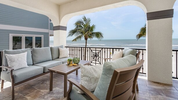 A balcony with a view of the ocean, a sofa, a table, and a chair. - Curious Tides - 3132/3134 Estero Blvd. 10 Bedroom Townhouse by RedAwning (Fort Myers Beach)