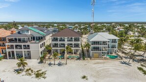 A beachfront property with multiple buildings, including a large house with a pool and a smaller building with a beach view. - Curious Tides - 3132/3134 Estero Blvd. 10 Bedroom Townhouse by RedAwning (Fort Myers Beach)