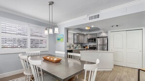 Una cocina moderna con armarios blancos, una isla central y un comedor con mesa gris y sillas blancas.