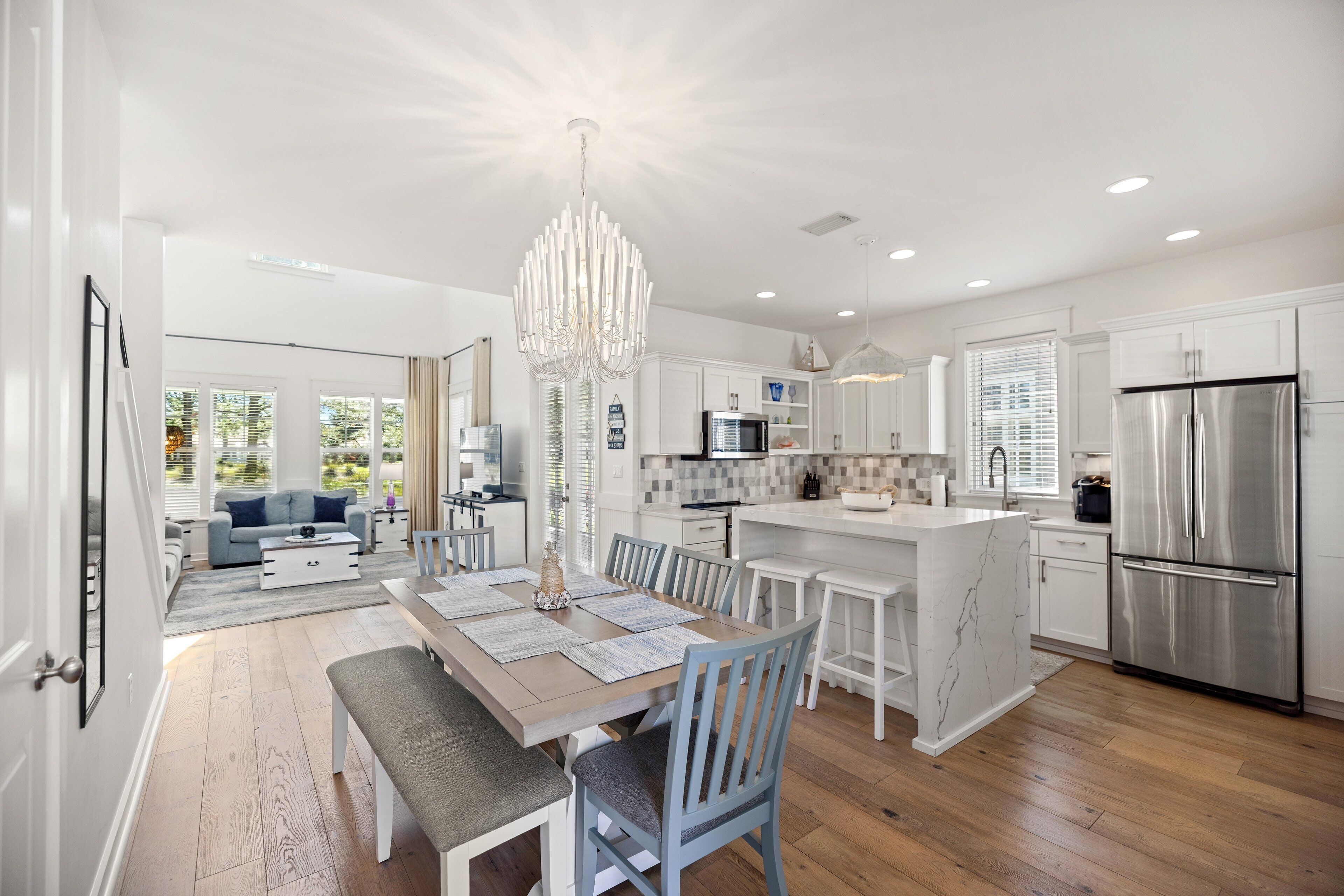A modern kitchen with white cabinetry, a stainless steel refrigerator, and a dining area with a bench and chairs.