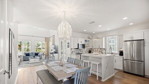 Une cuisine moderne avec des meubles blancs, un réfrigérateur en acier inoxydable et un coin repas comprenant une banquette et des chaises.