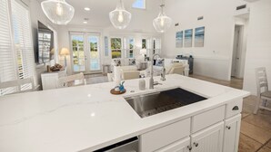 Una cocina amplia con una isla grande, armarios blancos e iluminación colgante.