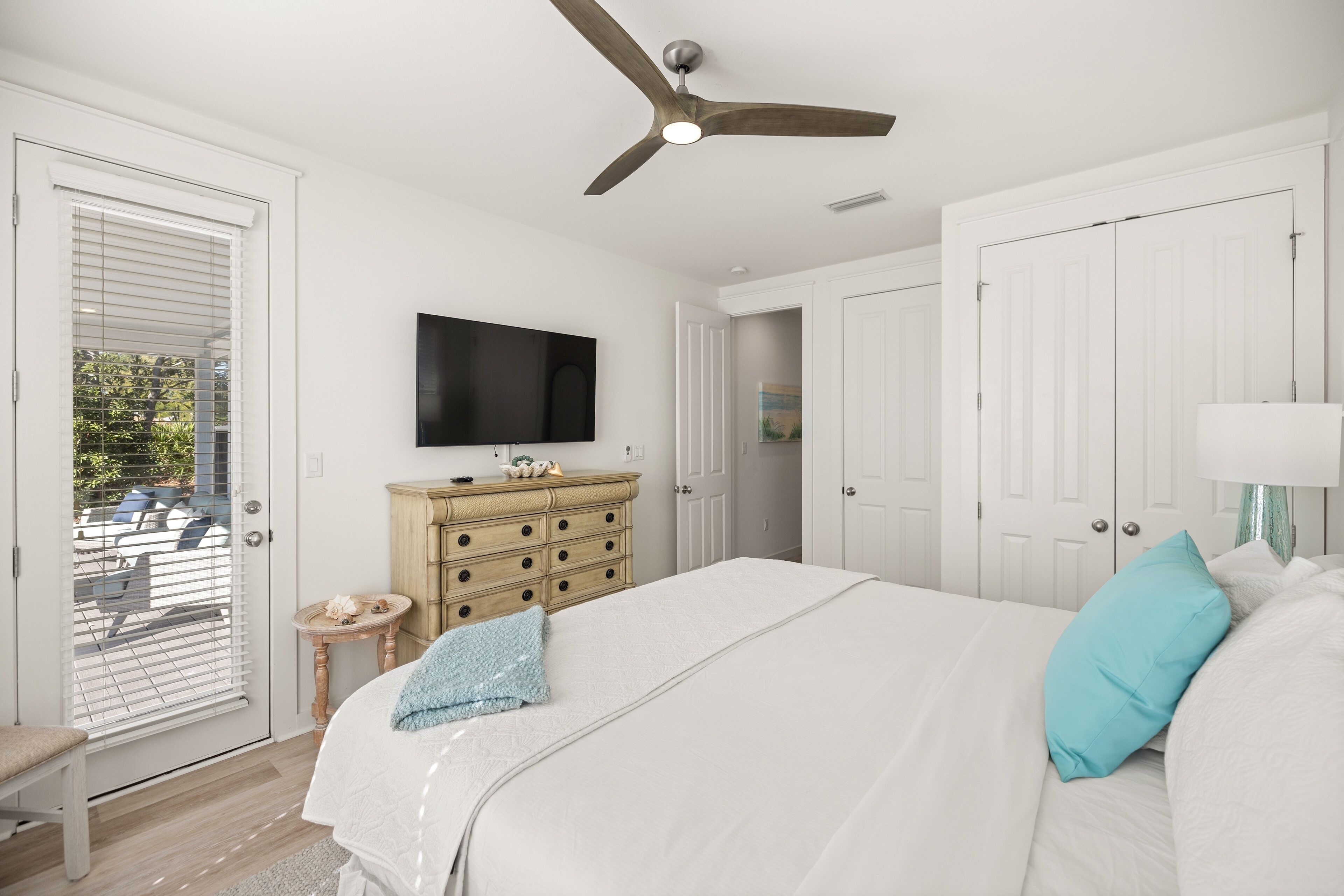 Un dormitorio con cama, ventilador de techo, televisión en la pared y puerta que da a un balcón.