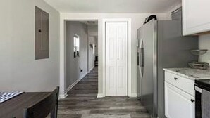 Ein schmaler Flur mit einer Holzbank, einer weißen Tür am Ende und einem Kühlschrank zur Rechten.