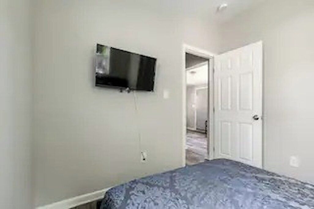 A bedroom with a bed, a television mounted on the wall, and a door leading to another room.
