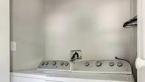 Ein kleiner Hauswirtschaftsraum mit einer Waschmaschine und einem Trockner mit Frontlader, einer kleinen Steckdose und einer Tür zu einem anderen Raum.