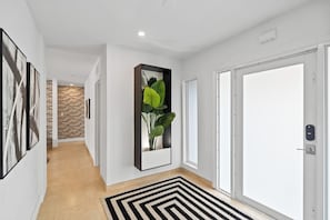A hallway with a black and white striped rug, a plant in a rectangular planter, and a brick wall in the background.