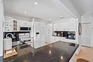 A modern kitchen with white cabinets, a large granite countertop, and stainless steel appliances. - Design Loft Home with Private Pool & BBQ, Sleeps 12, 15 Min to MIA (Miami)