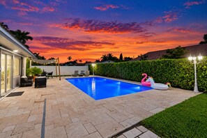A swimming pool with lounge chairs and a flamingo float, surrounded by a hedge and a lamp post.