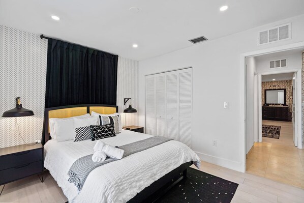 A modern bedroom with a bed, bedside tables, a wardrobe, and a bathroom visible through an open door.