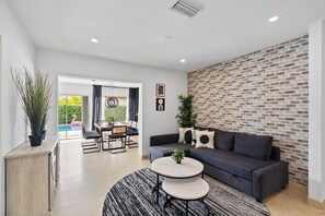 A modern living room with a grey sofa, a round coffee table, and a dining area with a table and chairs.