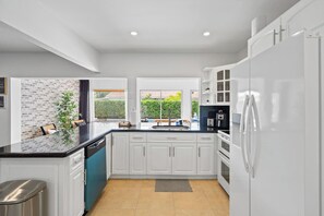 A modern kitchen with white cabinets, a black countertop, and a stainless steel refrigerator.