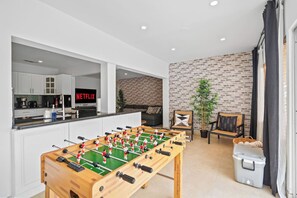 A modern living space with a foosball table, a kitchen area, a brick wall, and a seating area with a sofa and chairs. - Design Loft Home with Private Pool & BBQ, Sleeps 12, 15 Min to MIA (Miami)