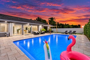 A swimming pool with a flamingo float, a covered patio area, and a house with sliding glass doors.