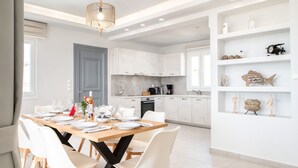 A modern kitchen with white cabinets, a dining area with a wooden table set for six, and a white shelving unit with decorative items.