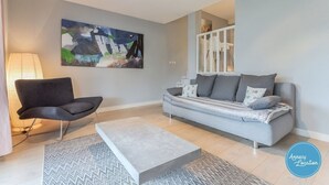 A modern living room with a grey sofa, a black armchair, and a painting on the wall.