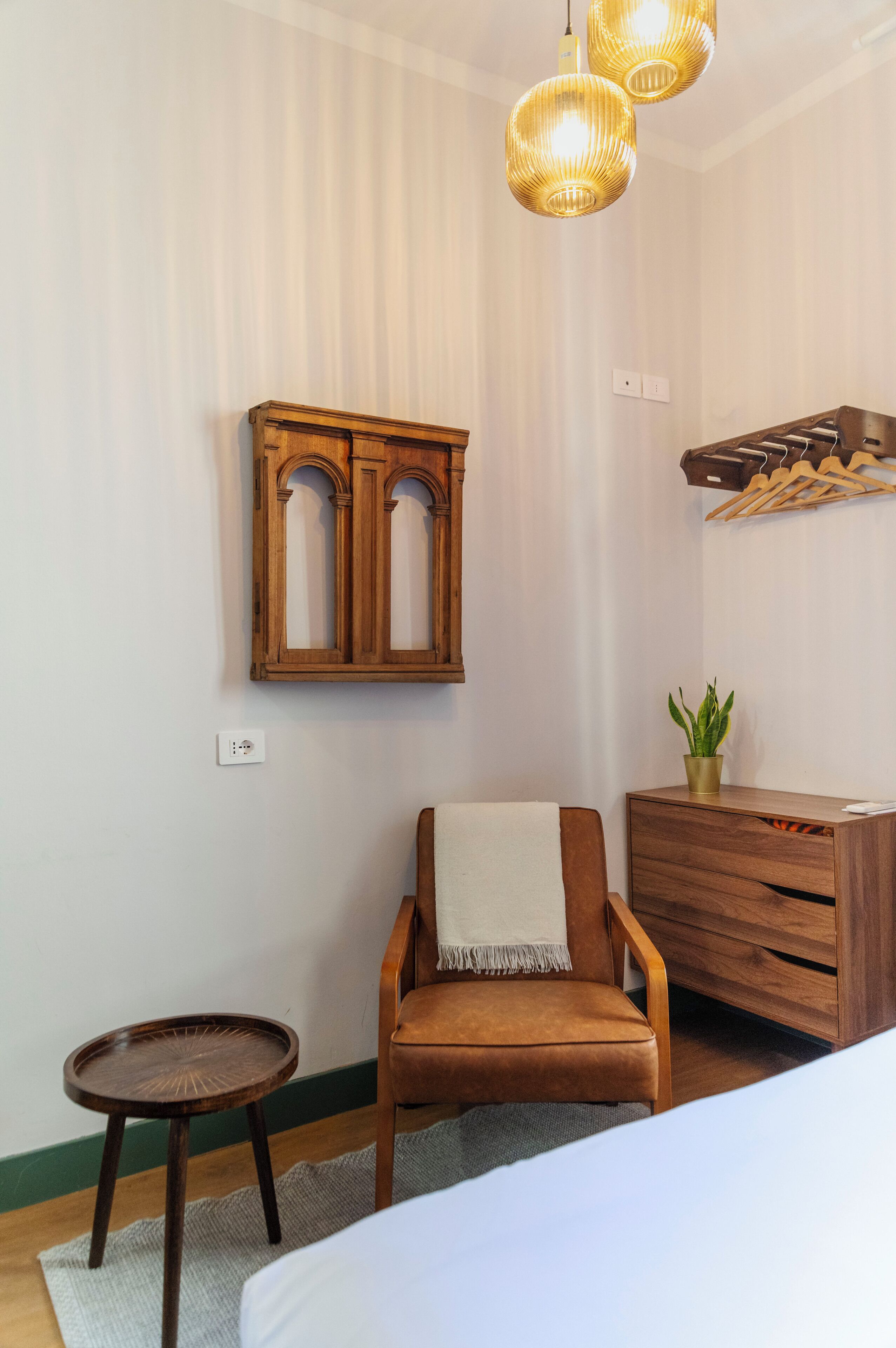 Una habitación con una cama, una silla de madera, una mesita redonda pequeña, un armario y una lámpara colgante.