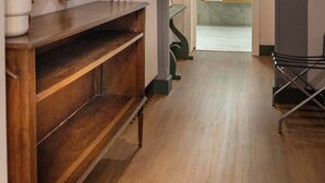 Un couloir avec une console en bois, un grand miroir et un radiateur. Une porte donne sur une salle de bain équipée d’un lavabo et d’un miroir.