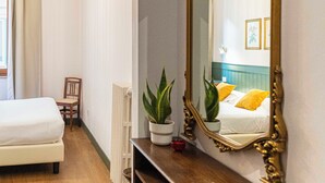 Une chambre à coucher avec un grand miroir décoratif, un lit, une petite table sur laquelle est posée une plante en pot et un radiateur.