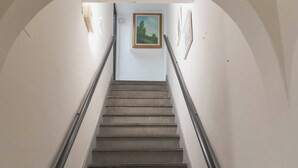 Un escalier muni d’une rampe, menant à un palier où est accroché un tableau encadré.