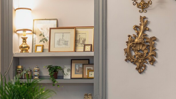 Une pièce comprenant deux fauteuils marron à revêtement en tissu, une petite table ronde, une plante en pot, un luminaire décoratif fixé au mur et une étagère avec des photos encadrées et des objets décoratifs.