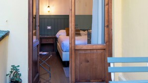 Une porte en bois qui donne sur une pièce contenant un lit, une petite table et un luminaire suspendu.