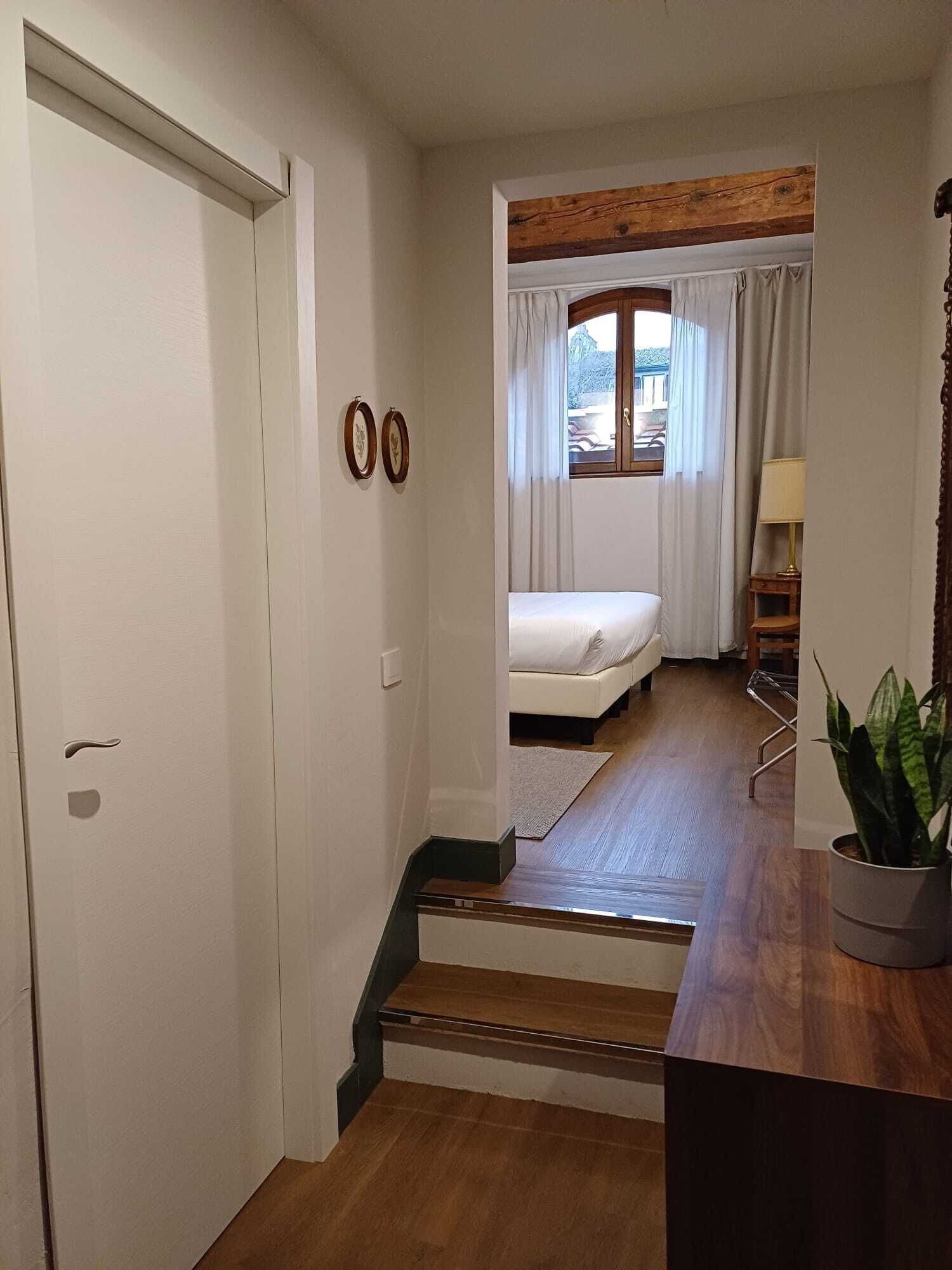 Un dormitorio con cama, una ventana con cortinas, una mesita de noche y una planta.