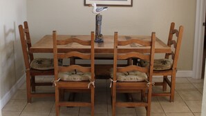 Uma mesa de jantar com seis cadeiras de madeira, um quadro na parede e um pequeno pássaro decorativo no centro da mesa.