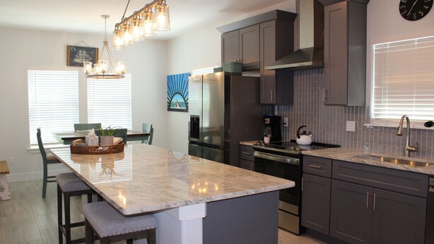 A modern kitchen with a marble island, stainless steel appliances, and a large clock on the wall.