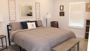 A bedroom with a bed, bedside table, lamp, chair, and window.