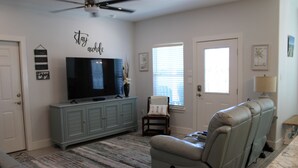 A living room with a flat-screen TV, grey sofa, and a ceiling fan.