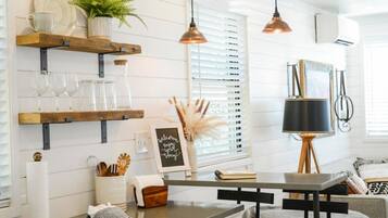 A kitchen with wooden shelves, a hanging pendant light, a wall-mounted air conditioner, and a framed welcome sign.