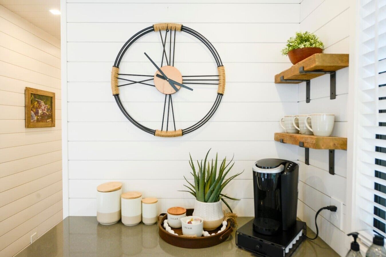 Een keuken met een hangend klokje, planken met mokken, een koffiezetapparaat en een plant.
