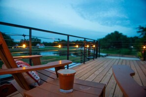 A wooden deck with a table and chairs, a glass of beer, and string lights. - Luxury Container Home | Pickleball | Rooftop Patio (Waco)