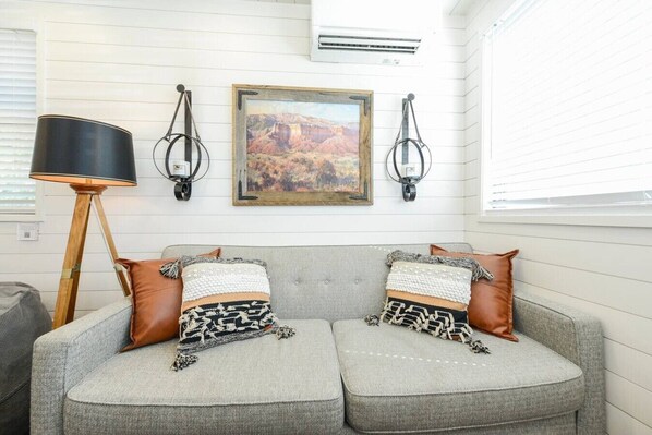 A grey sofa with two patterned cushions, a black floor lamp, and a framed painting of a desert landscape.