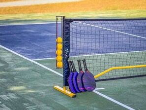 A tennis court with a net, a ball machine, and tennis rackets. - Luxury Container Home | Pickleball | Rooftop Patio (Waco)
