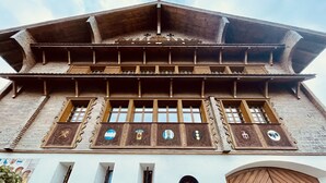 En byggnad med en traditionell arkitektonisk stil, med en träfasad, flera fönster med dekorativa detaljer och en framträdande trädörr.