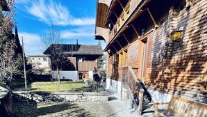 En innergård med kullerstenar, en träbänk, en stenmur och en byggnad med träbalkonger.