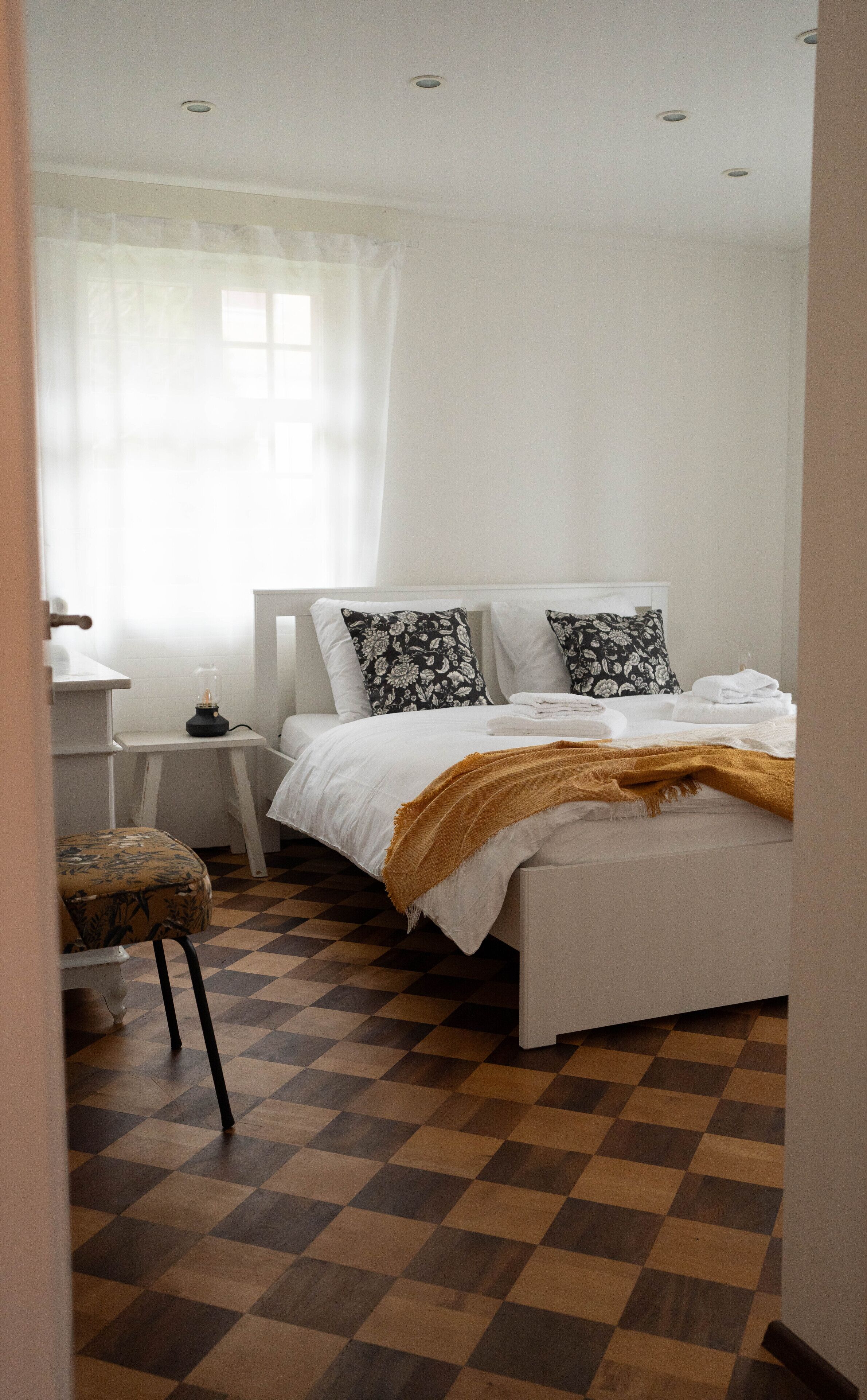 Ein Schlafzimmer mit einem Bett, einem Nachttisch, einer Lampe, einem Sessel und einem karierten Boden.