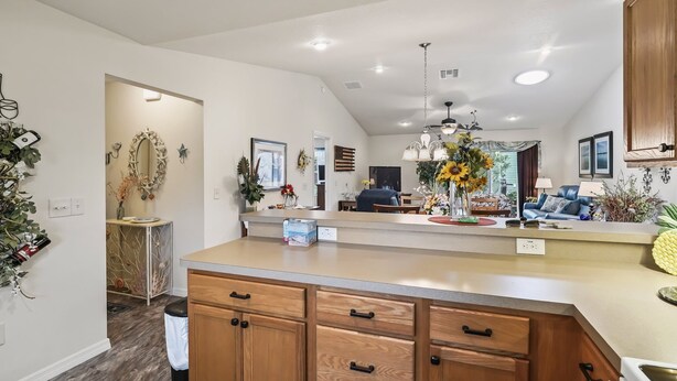 A modern kitchen with wooden cabinets, a central island, and a dining area with a sofa and table. - Charming 3BR Ranch in Sanibel Village: Your Ultimate Florida Getaway! (The Villages)