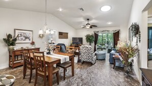 A spacious living area with a dining table, chairs, a sofa, and a TV. There are plants and a ceiling fan. - Charming 3BR Ranch in Sanibel Village: Your Ultimate Florida Getaway! (The Villages)
