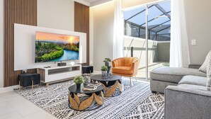 A modern living room with a flat-screen TV, a grey sofa, a round coffee table, and a patterned rug. - 4BR/3BA Disney-Themed Townhome at Storey Lake (Kissimmee)