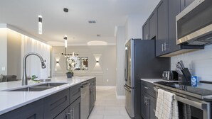 A modern kitchen with dark cabinets, stainless steel appliances, and a large island with a sink. - 4BR/3BA Disney-Themed Townhome at Storey Lake (Kissimmee)