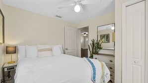 Une chambre d’hôtel comprenant un lit, une table de chevet, une lampe, une commode, un miroir et un ventilateur de plafond.