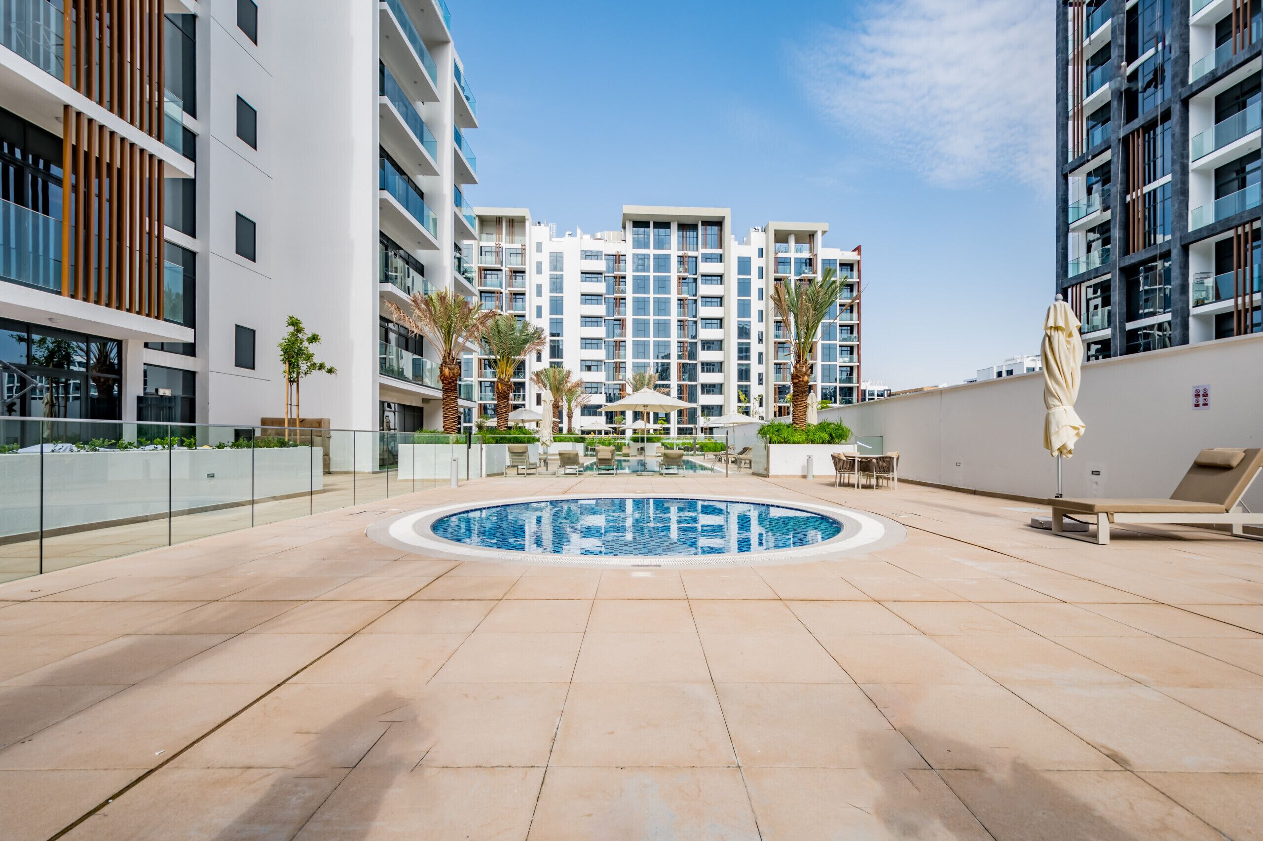 A modern outdoor pool area with a circular pool, lounge chairs, and a view of high-rise residential buildings.