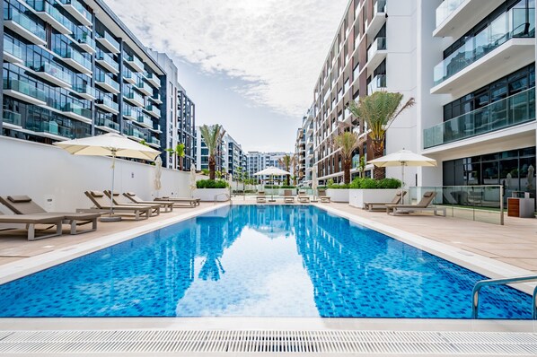 Une piscine entourée de bâtiments modernes dotés de balcons, avec des chaises longues et des parasols à proximité.