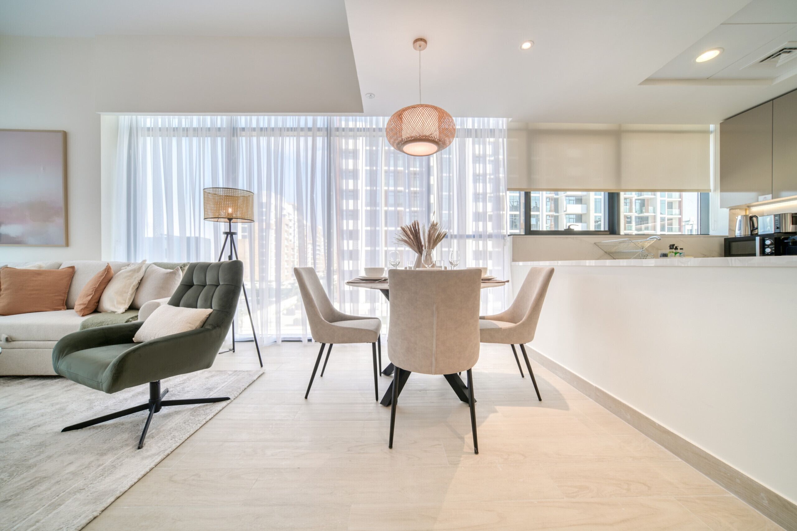 Uma sala de estar moderna com sofá, mesa de jantar com cadeiras, luminária de chão e área de cozinha com bancada e eletrodomésticos.