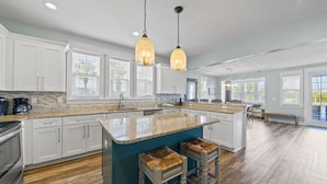 A spacious kitchen with white cabinets, a granite countertop, and a large island with stools. - Stunning Lake Views in Miramar! Golf Cart, Splash Pool, Private Beach Access! (Miramar Beach)