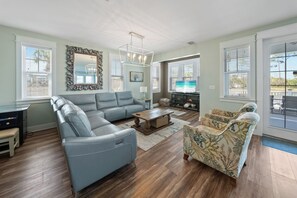 A spacious living room with a sectional sofa, a patterned armchair, a coffee table, and a TV.