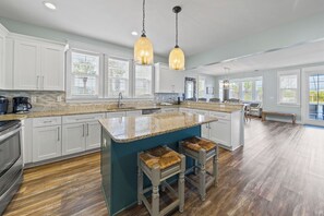 A spacious kitchen with white cabinets, a granite countertop, and a large island with stools.